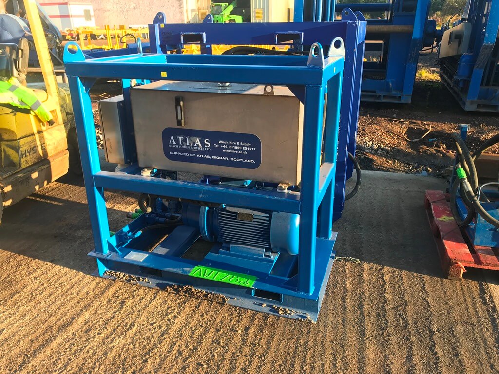 Blue industrial equipment with an Atlas label sits on a concrete floor, surrounded by machinery.