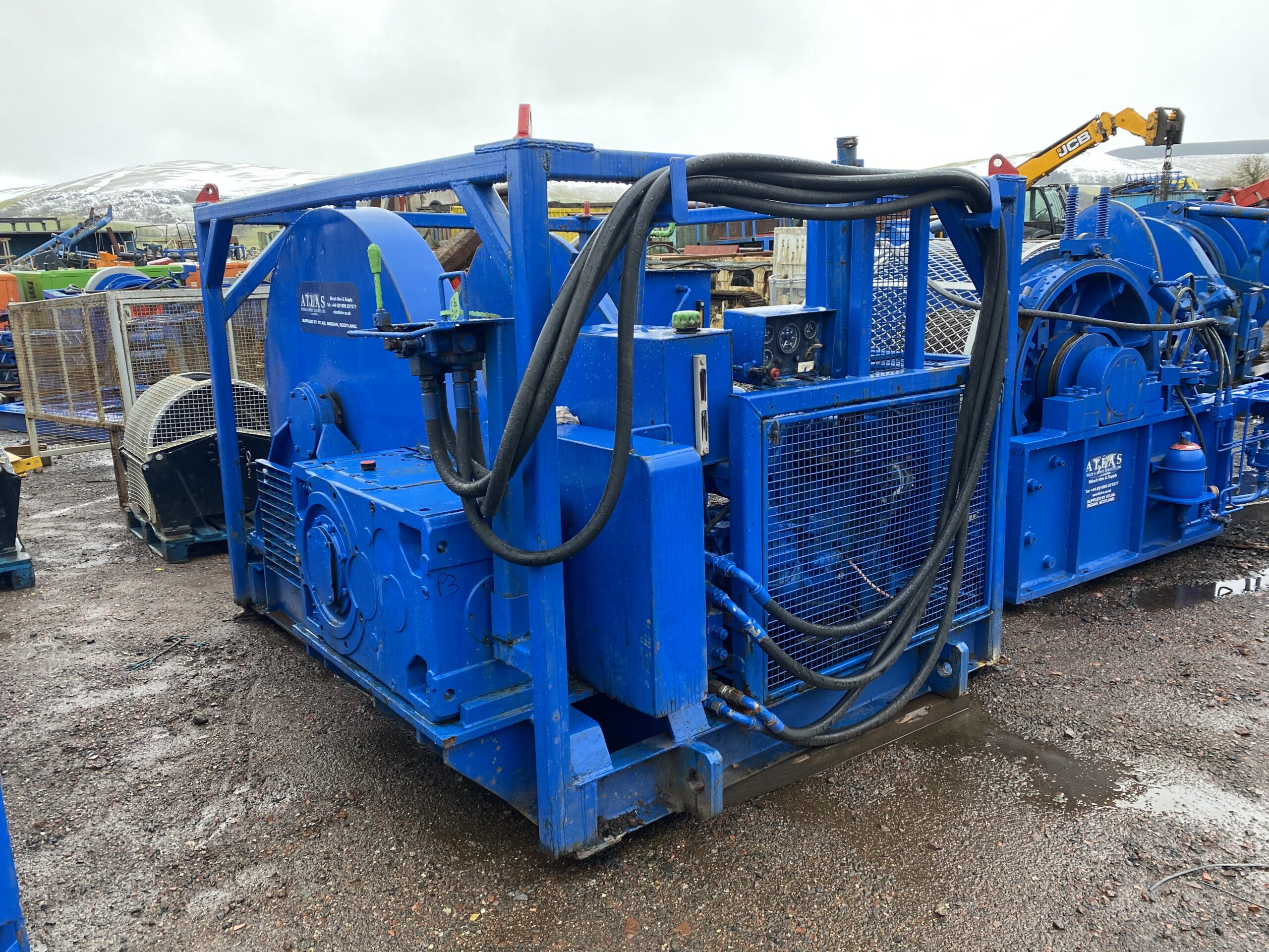 A large blue industrial machine with visible hoses and control panels sits on a muddy ground.