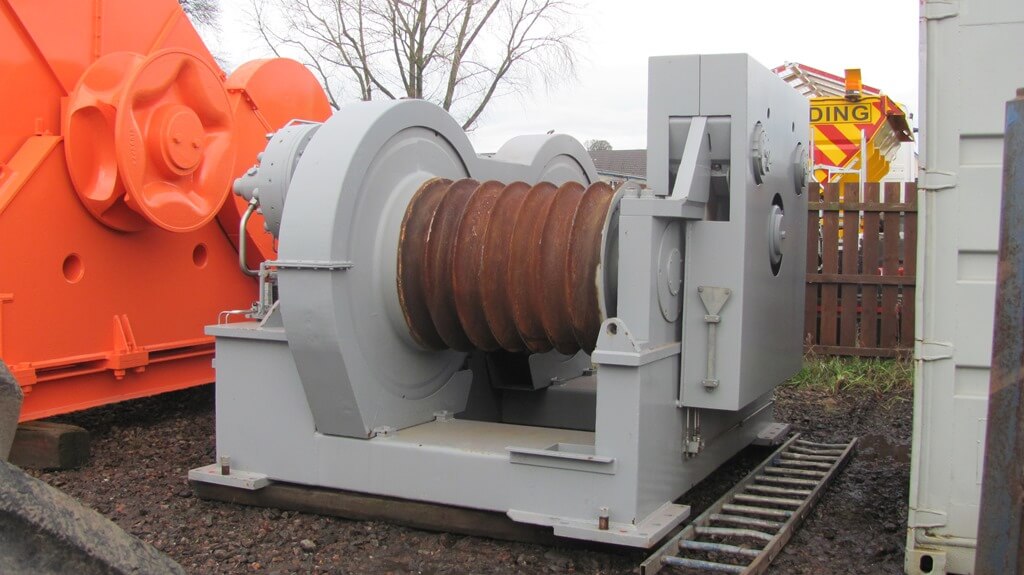 Large industrial winch with a cable drum, set on a metal platform.