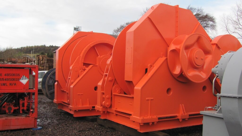 Bright orange industrial winches with large wheels is stacked on the ground outdoors.